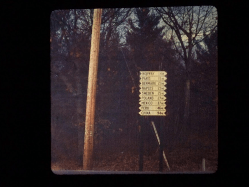 A weathered signpost with directional arrows pointing to various countries and their distances in miles.