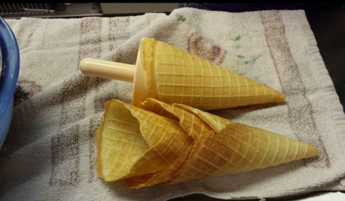 Two empty ice cream cones resting on a textured towel, one cone stacked inside the other.