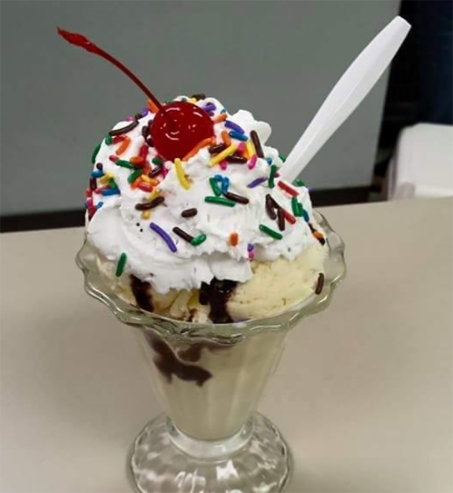 A delicious ice cream sundae topped with whipped cream, colorful sprinkles, and a cherry in a glass dish.
