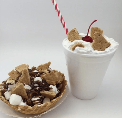 A dessert bowl with chocolate, marshmallows, and graham cracker pieces next to a whipped cream topped drink with a cherry.