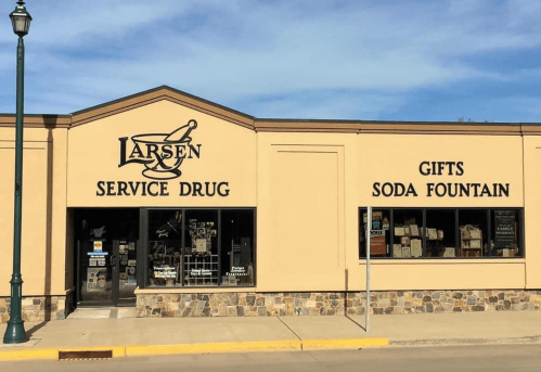 Exterior of Larsen Service Drug, featuring a soda fountain and gift shop, with a clear blue sky above.