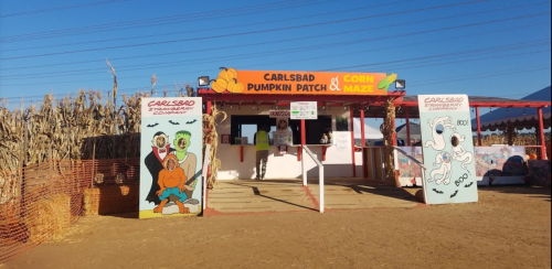 Entrance to the Carlsbad Pumpkin Patch, featuring a colorful sign and decorations, with corn maze in the background.