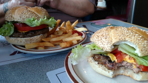 Two large sesame seed burgers with lettuce, tomato, and cheese, served with a side of golden French fries.