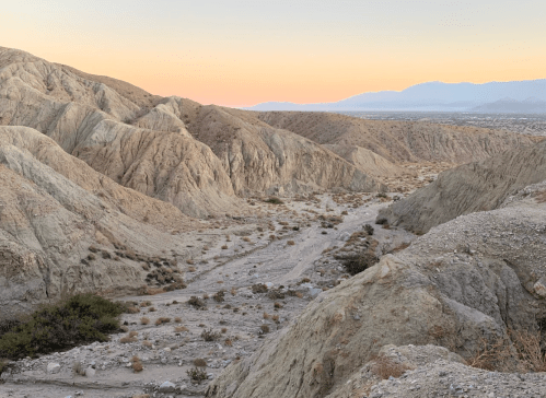 A desert landscape with rugged hills and a soft sunset glow in the background, showcasing a dry, arid terrain.