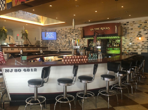 A stylish bar with a curved counter, high stools, and a wall of colorful tiles, featuring a TV displaying "Music of the Stars."