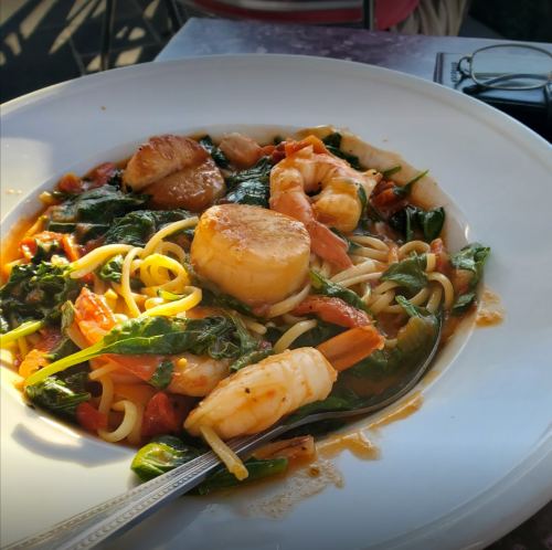 A plate of pasta with shrimp, scallops, spinach, and tomatoes, garnished with a silver spoon.