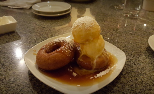 A plate with two donuts topped with a scoop of ice cream and drizzled with caramel sauce, dusted with powdered sugar.