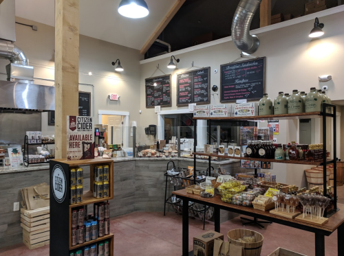 Interior of a market featuring shelves of snacks, beverages, and a menu board, with a rustic wooden display.