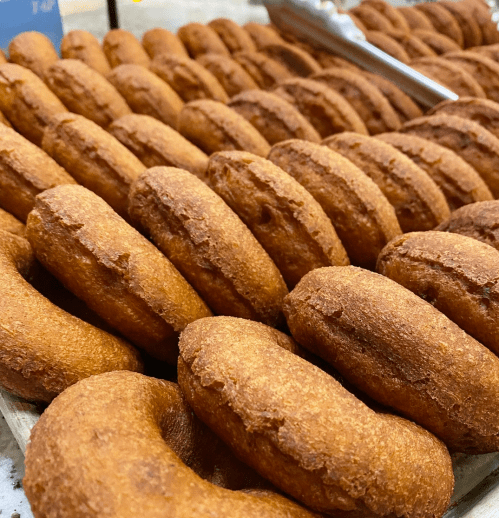 A close-up of freshly baked, golden-brown donuts arranged in neat rows on a display tray.