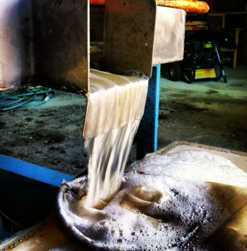 Water flows from a metal spout into a container, creating bubbles and foam on the surface.