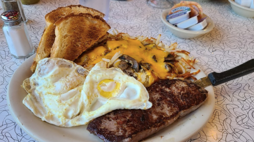 A plate of breakfast featuring steak, eggs, cheesy hash browns, and toast on a patterned table.