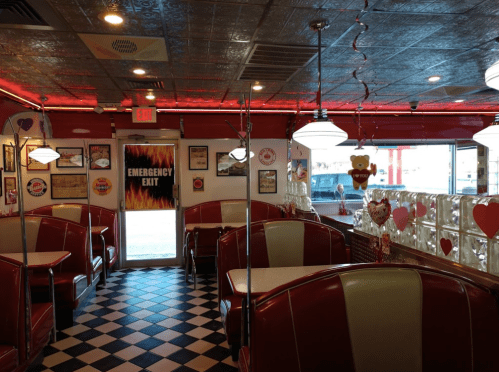 A retro diner interior with red booths, checkered floor, and heart decorations, featuring an emergency exit door.