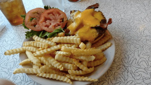 A plate of crinkle-cut fries with a cheeseburger topped with melted cheese, lettuce, and tomato slices on the side.