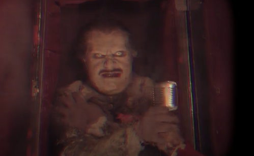 A creepy clown figure with a microphone, appearing through a dark, foggy backdrop.