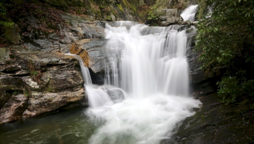 A serene waterfall cascading over rocky terrain into a calm pool, surrounded by lush greenery.