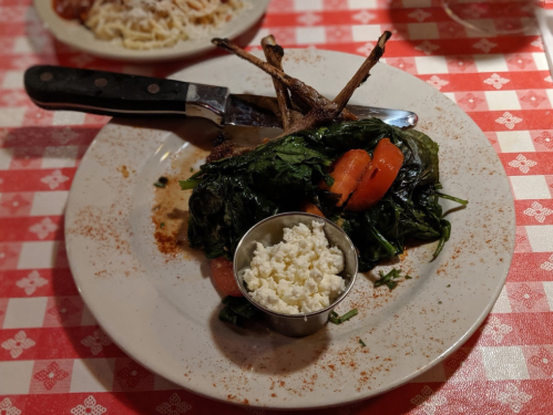 A plate with sautéed greens, carrots, and a small bowl of cheese, garnished with a fork and knife on a checkered tablecloth.