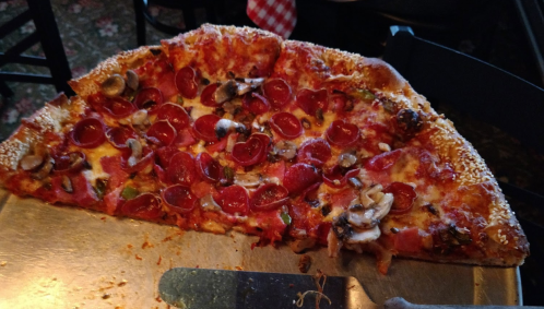 A large slice of pepperoni pizza topped with mushrooms and herbs on a metal tray.
