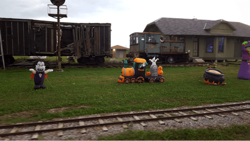 Inflatable Halloween decorations, including a train and spooky characters, set against a backdrop of old train cars and a house.