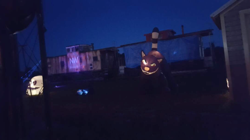 A dark outdoor scene featuring Halloween decorations, including a large inflatable cat and ghostly figures.