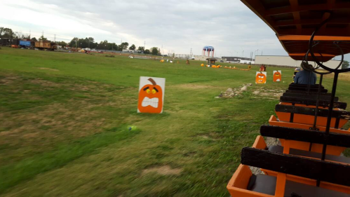 A view of a grassy field with pumpkin decorations and a train ride in the foreground, under a cloudy sky.