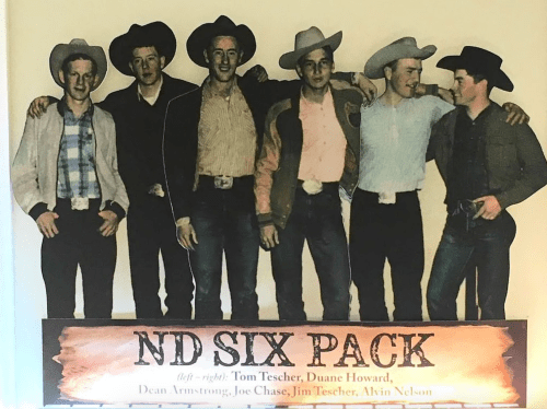 A group of six cowboys in hats and western attire, posing together with a sign reading "ND Six Pack."