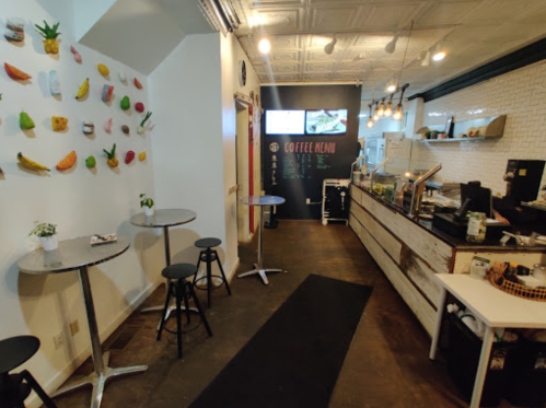 A cozy coffee shop interior featuring a colorful wall display, a counter with a menu, and small tables with stools.