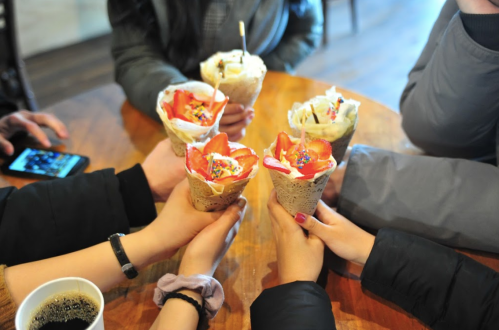 A group of hands holding colorful ice cream cones decorated with flowers and sprinkles, gathered around a wooden table.