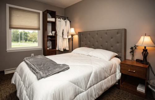 Cozy bedroom with a queen bed, gray accents, a nightstand, and a window with natural light.