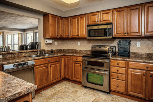 A modern kitchen with wooden cabinets, granite countertops, stainless steel appliances, and a tiled floor.