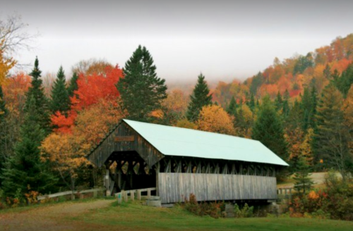 A rustic covered bridge surrounded by vibrant autumn foliage and misty mountains in the background.