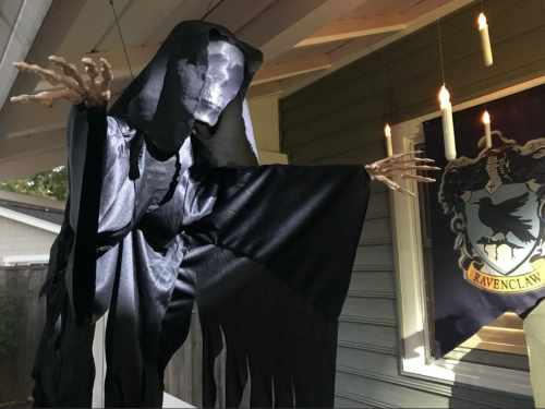 A spooky black cloaked figure with skeletal hands hangs under candles, set against a wall with a Ravenclaw banner.