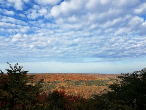 A scenic view of rolling hills covered in autumn foliage under a partly cloudy sky.