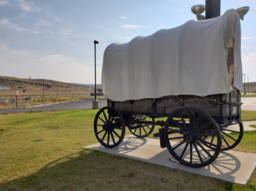 A covered wagon on display, set against a vast, open landscape under a clear sky.