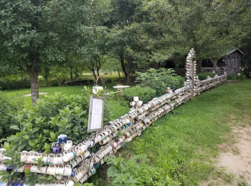 A whimsical fence made of colorful mugs, surrounded by greenery and trees in a serene outdoor setting.