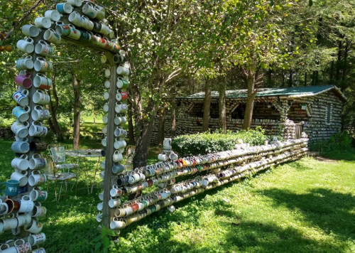 A whimsical outdoor scene featuring a mug-adorned fence and a rustic building surrounded by greenery.