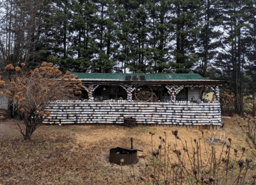 A rustic building with a green roof, decorated with colorful plates, surrounded by trees and a grassy area.