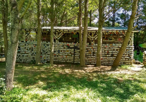 A rustic building surrounded by trees, its walls covered with colorful cups and plates, creating a unique artistic display.