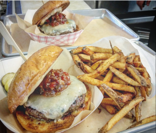 A juicy burger with melted cheese and toppings, served with a side of crispy fries on a tray.