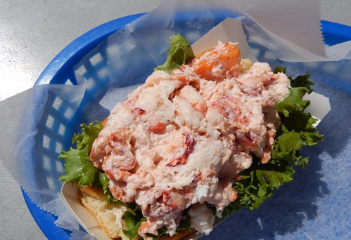 A lobster roll piled high with lobster meat on a bed of lettuce, served in a blue basket.