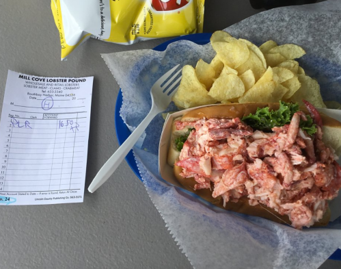 A lobster roll with lettuce and potato chips on a blue plate, next to a receipt from Mill Cove Lobster Pound.