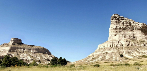 Two large, rocky formations rise against a clear blue sky, surrounded by grassy plains.