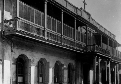Historic building with balconies and shutters, featuring a cross on the roof, captured in black and white.