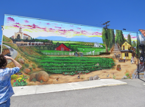 A colorful mural depicting a rural landscape with farms, fields, and a historic building under a blue sky.