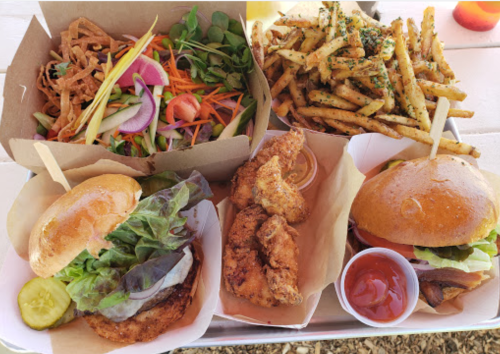 A spread of food featuring two burgers, fried chicken, a salad, and seasoned fries on a table.