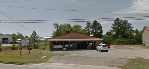 A small storefront with a red roof, surrounded by trees and power lines, on a sunny day.