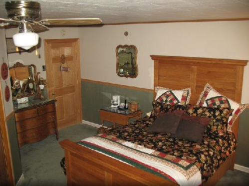 Cozy bedroom featuring a wooden bed, floral bedding, a dresser, and a mirror, with warm, inviting decor.