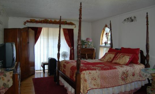 A cozy bedroom featuring a four-poster bed, floral bedding, wooden furniture, and large windows with curtains.