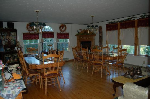 A spacious dining room with wooden chairs, a large table, and windows adorned with red curtains.