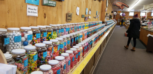 A colorful display of jars filled with various candies, with a person browsing in a cozy shop.
