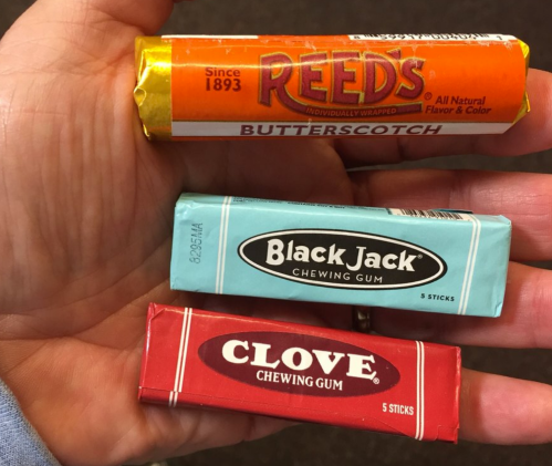 A hand holding three types of retro candies: Reeds Butterscotch, Black Jack gum, and Clove gum, all in colorful wrappers.